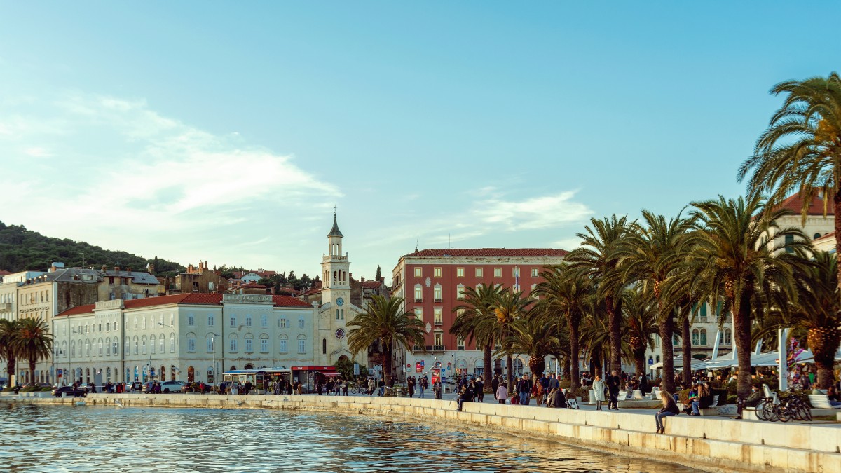 Menschen auf der Riva in Split, Kroatien, die entlang der Uferpromenade am Meer spazieren.