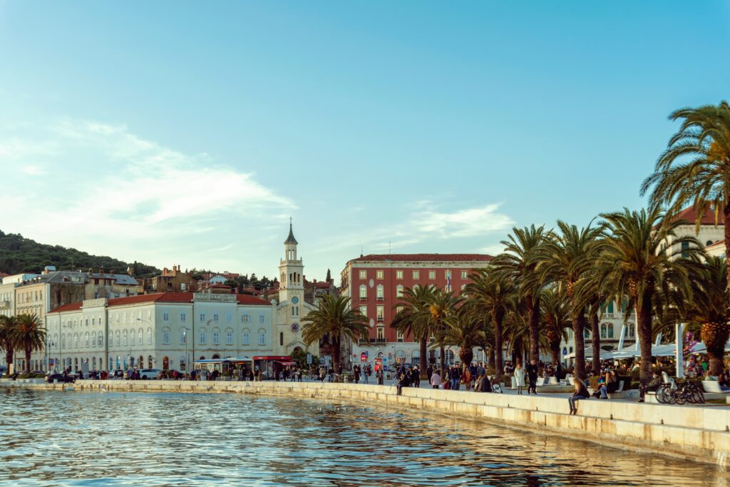 Promenade "Riva" in Split, Kroatien, mit Menschen, Palmen und Blick auf alte Bauten.