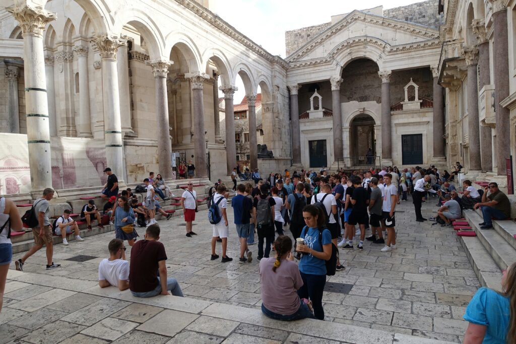 Menschen im Peristil des Diokletianpalastes in Split, Kroatien, die auf den Stufen sitzen und sich unterhalten.