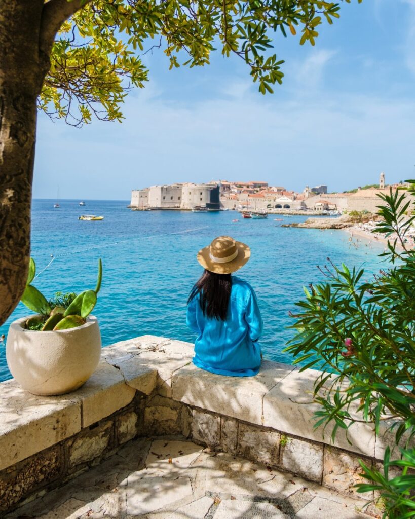 Person mit Sonnenhut sitzt am Meer Mit Blick auf die Altstadt von Dubrovnik in Kroatien