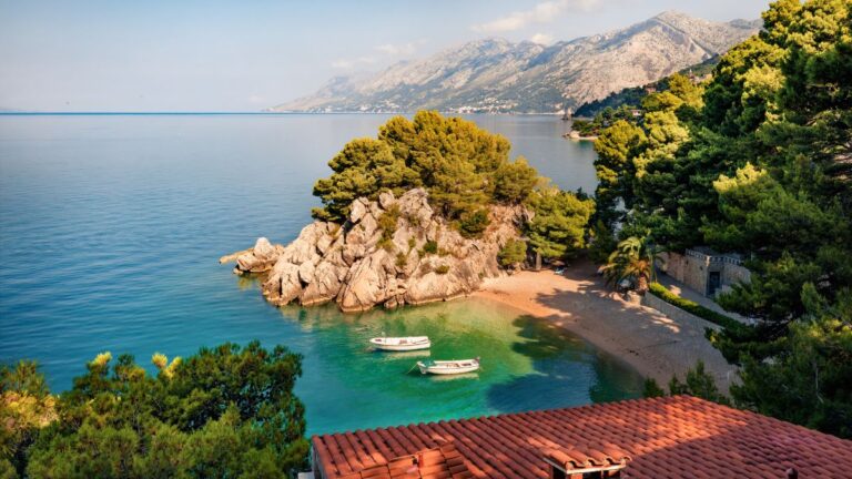 Bucht bei Bela an der Makarska Riviera mit grün schimmerndem Wasser, Pinien, Felsen und dem Bikovo-Gebirge im Hintergrund.