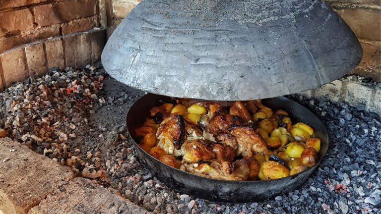 Traditionelle Peka in Kroatien mit Fleisch und Kartoffeln unter einer schweren Metallhaube in einer Feuerstelle mit Glut.